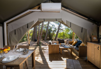 Innenansicht des Safari-Zelts Comfort mit Klimaanlage, Esstisch und gemütlicher Sitzecke im Grünen.