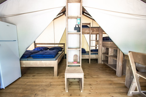 Interior de la Safari Tent Comfort con piso de madera, cama doble, literas y un refrigerador.