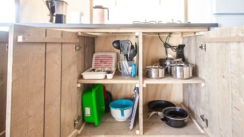 Küchenschrank im Safari Tent Comfort mit Töpfen, Utensilien, Geschirr und Besteck auf Regalen.