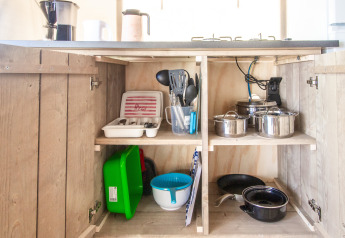 Küchenschrank im Safari Tent Comfort mit Töpfen, Utensilien, Geschirr und Besteck auf Regalen.