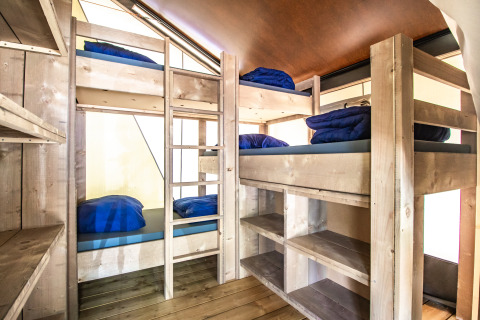 Interno di Safari Tent Comfort con quattro letti a castello in legno chiaro, coperte blu e scaffali integrati.