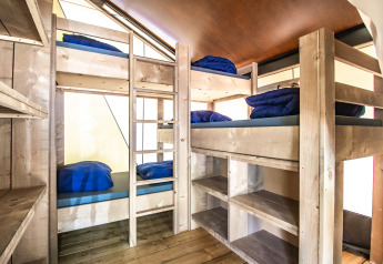 Interior de la Safari Tent Comfort con cuatro literas de madera clara, ropa de cama azul y estanterías integradas.