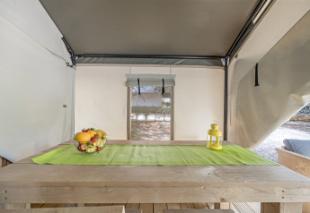 Interieur van de Safari Tent Comfort op Camping Porto Sole in Kroatië met houten tafel en fruitmand.