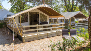 Vista exterior de una Safari Tent Luxury con terraza de madera, tumbonas y rodeada de vegetación.