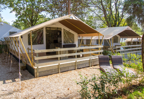 Außenaufnahme eines luxuriösen Safari-Zeltes mit Holzterrasse und Sonnenliegen in natürlicher Umgebung.