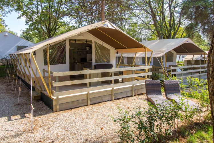 Vue extérieure d'une Safari Tent Luxury avec terrasse en bois, transats et entourée de verdure.