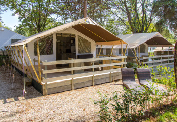 Vista exterior de una Safari Tent Luxury con terraza de madera, tumbonas y rodeada de vegetación.
