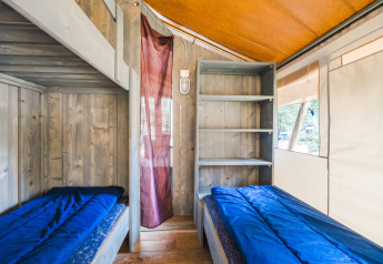 Interior de la Safari Tent Luxury en Camping Valkanela, Croacia, con dos camas y estantería de madera.