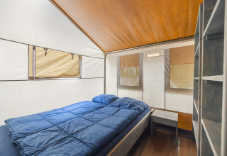 Vista interior de Safari Tent Luxury con cama doble, mesita de noche y estantería en Camping Valkanela en Croacia.