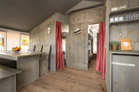 Interno di una Safari Tent Luxury al Camping Lanterna in Croazia con arredi in legno e tende rosse.