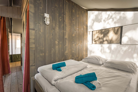 Interno di una tenda safari luxury al Camping Lanterna in Croazia con letto matrimoniale e asciugamani puliti.