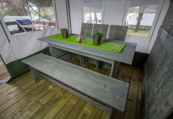 Set da pranzo nel Safari Tent Luxury al Camping Lanterna, Croazia, con panca di legno e tovaglia verde.