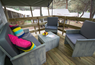 Outdoor seating with gray chairs and colorful pillows on the deck of Safari Tent Luxury at Camping Lanterna.