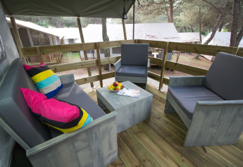 Outdoor seating with gray chairs and colorful pillows on the deck of Safari Tent Luxury at Camping Lanterna.
