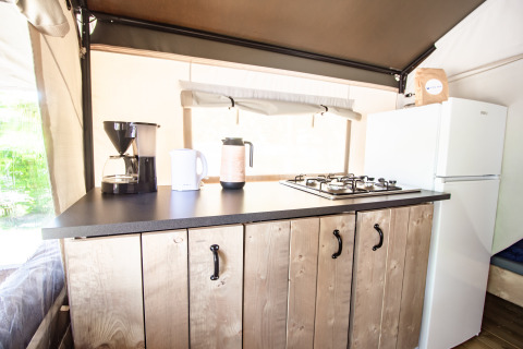 Cocina de Safari Tent Comfort con estufa de gas, cafetera, hervidor y nevera sobre gabinetes de madera.