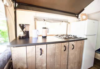 Cocina de Safari Tent Comfort con estufa de gas, cafetera, hervidor y nevera sobre gabinetes de madera.