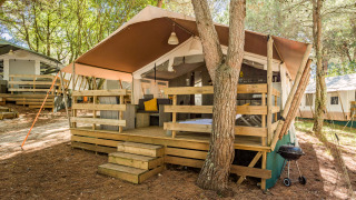 Luxe safaritent met houten veranda, zitgedeelte en barbecue, gelegen op een rustige bosrijke camping.