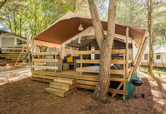 Luxe safaritent met houten veranda, zitgedeelte en barbecue, gelegen op een rustige bosrijke camping.
