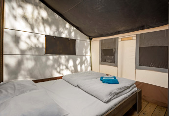Binnenaanzicht van een luxe safaritent met tweepersoonsbed bij Camping Lanterna in Kroatië, zonlicht.