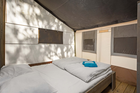 Vista interior de una tienda safari de lujo con cama doble en Camping Lanterna, Croacia, con luz solar.