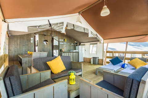 Interior de tienda safari de lujo en Camping Lanterna, Croacia, con muebles de madera y cojines de colores.