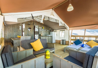 Interior de tienda safari de lujo en Camping Lanterna, Croacia, con muebles de madera y cojines de colores.