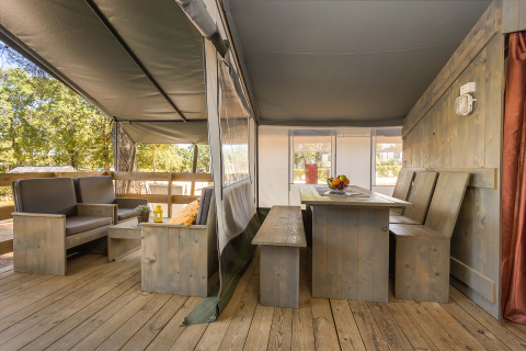 Área interior de Safari Tent Luxury en Camping Lanterna, Croacia, con muebles de madera y asientos cubiertos.