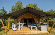 Safari tent Comfort met airconditioning, houten veranda, tuinmeubilair, tafel en stoelen in groene omgeving.