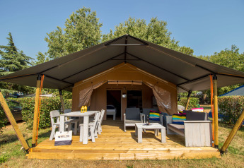 Safari tent Comfort met airco, houten terras, zithoek, tafel en stoelen in een groene, relaxte omgeving.