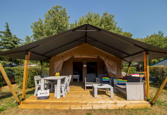 Safari tent Comfort with air conditioning, wooden deck, outdoor seating, table, chairs, and lush surroundings.