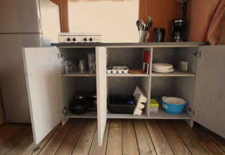 Køkkenskab med åben låge, fyldt med service og køkkenredskaber i en safari-telt på Camping Porto Sole.