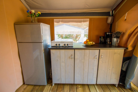 Zona de cocina en una tienda safari con nevera, cocina y armarios en Camping Porto Sole, Croacia.
