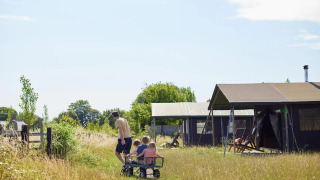 Familie aan de safaritent op Feather Down Glastonbury Hill Farm, Verenigd Koninkrijk, op zonnige dag.