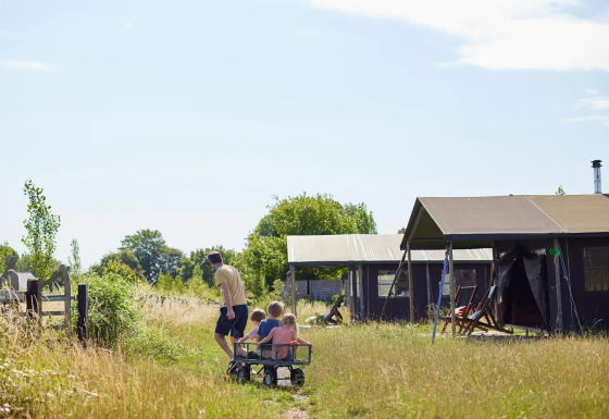 Familia junto a tienda safari en Feather Down Glastonbury Hill Farm, Reino Unido, en un día soleado.
