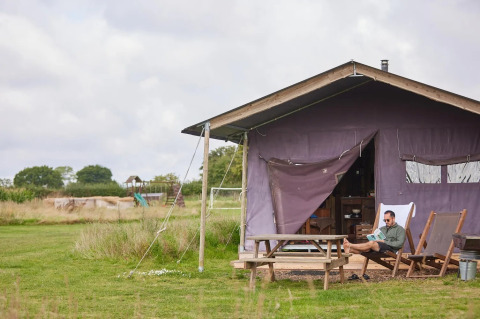 Homme détendu devant une tente safari avec douche privée à Feather Down New Barn Farm, Royaume-Uni.
