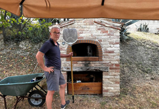 Mand står med pizzaspade foran en udendørs stenovn ved Agriturismo Angeli Sognanti i Marche, Italien.
