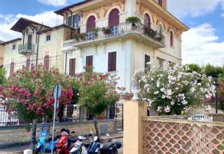 Elegante Villa mit verzierten Fenstern, Blumenbäumen und Motorrollern in Marche, Italien, bei Sonne.
