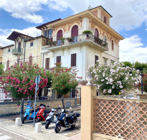 Charming villa with closed shutters, blooming trees and parked scooters in Marche, Italy, on a sunny day.