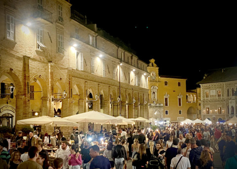 Mercado nocturno con multitudes y edificios iluminados en Agriturismo Angeli Sognanti, Marche, Italia.