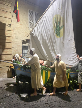 Personas con trajes tradicionales empujan un barco con vela por una calle adoquinada en Cossignano, Marche.