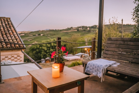 Avondzicht Agriturismo Angeli Sognanti in Marche, Italië, met houten bank, kaarsje, plaid en landschap.