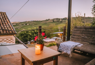 Avondzicht Agriturismo Angeli Sognanti in Marche, Italië, met houten bank, kaarsje, plaid en landschap.