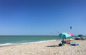 Stenstrand med farverige parasoller og kitere i vandet ved Agriturismo Angeli Sognanti, Marche, Italien.