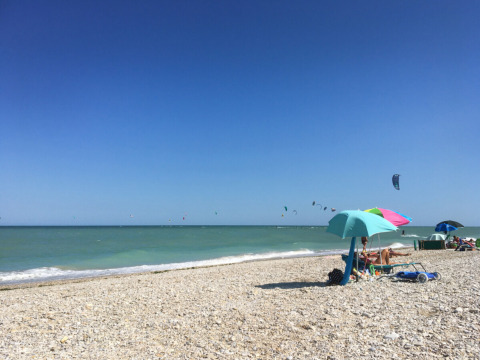 Kiezelstrand, kleurrijke parasols en kitesurfers bij Agriturismo Angeli Sognanti, Marche, Italië.