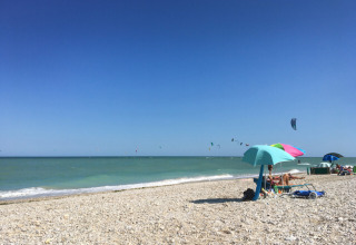 Pebble beach with colorful umbrellas and kite surfers at Agriturismo Angeli Sognanti, Marche, Italy.