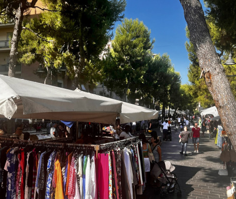 Buitenmarkt met kledingstanden en mensen onder bomen in Marche, Italië, vlakbij Agriturismo Angeli Sognanti.