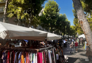 Mercato all'aperto con bancarelle di abbigliamento e persone tra gli alberi a Marche, Italia, vicino Angeli Sognanti.