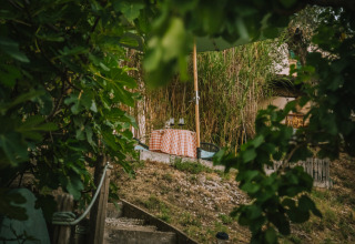 Zicht tussen groene bladeren op een sfeervolle tafel met ruitjeslaken bij Agriturismo Angeli Sognanti, Marche, Italië.