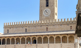 Edificio medieval con torre del reloj y arcos en una plaza cerca de Cossignano, región de Marche, Italia.