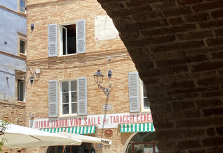 Vue à travers une arche en pierre sur une place et un café à Cossignano, dans les Marches, en Italie, par beau temps.